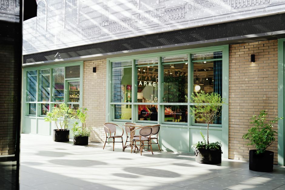 A modern retail unit located at Tottenham Hale Retail Park features a light brown brick façade with large green-framed windows that allow natural light to illuminate the interior. Outside, a small gar